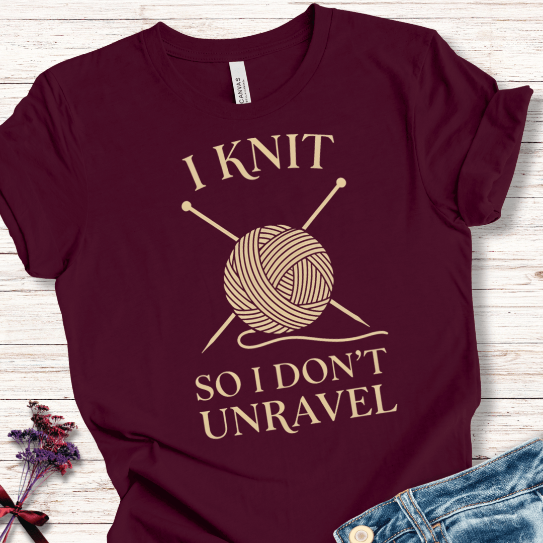 Maroon knit shirt with humorous text 'I Knit So I Don't Unravel' and yarn graphic for knitting enthusiasts.