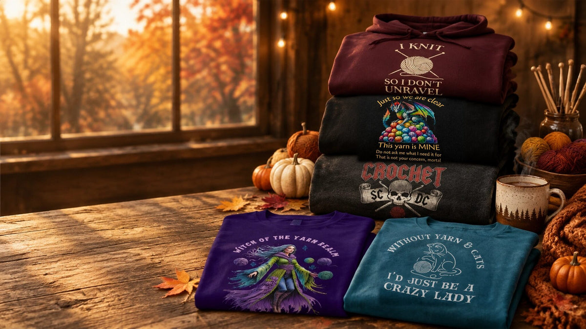 Our best sellers folded on an autumn table: the I Knit So I Don't Unravel hoodie, Yarn Dragon, SC DC Crochet Rock, Witch of the Yarn Realm and Cats & Yarn t-shirts