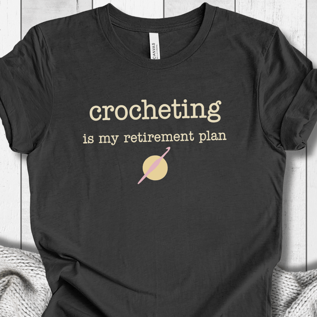 Black t-shirt featuring 'crocheting is my retirement plan' slogan, soft fabric, perfect for crochet lovers.