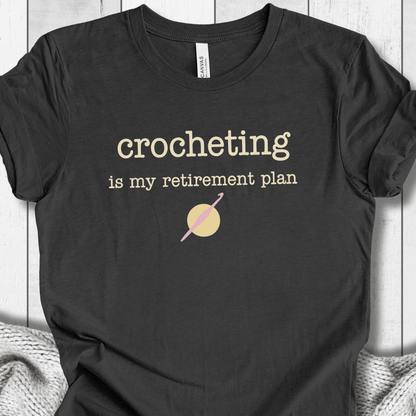 Black t-shirt featuring 'crocheting is my retirement plan' slogan, soft fabric, perfect for crochet lovers.