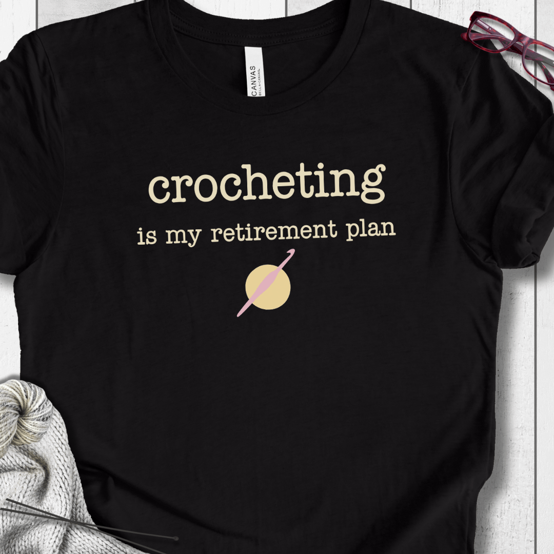 Black cotton t-shirt with 'crocheting is my retirement plan' slogan and crochet hook graphic.
