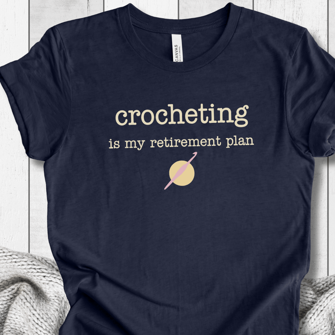 Navy blue t-shirt with 'Crocheting is my retirement plan' graphic on soft fabric.