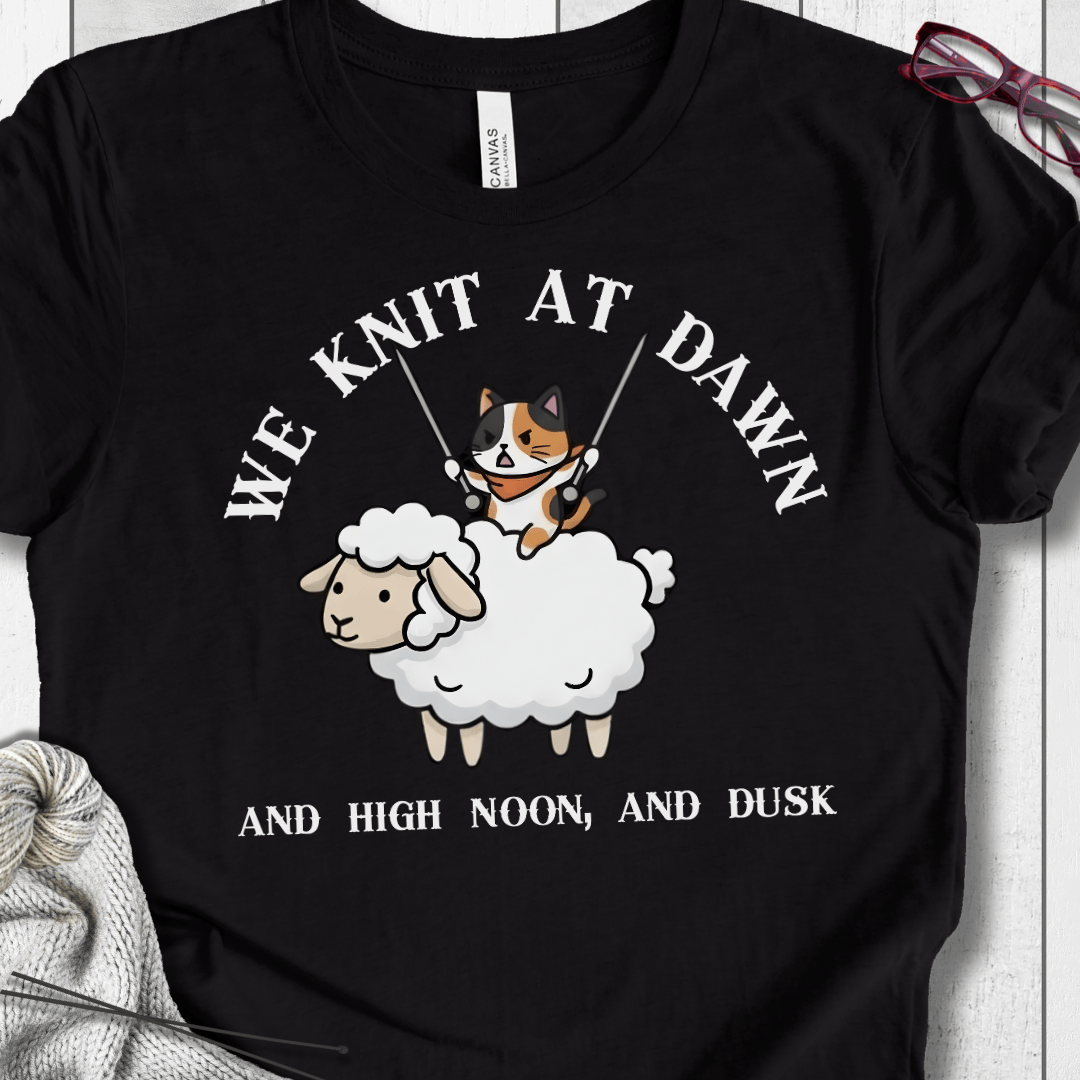 Funny black t-shirt featuring a cat knitting on a sheep, with the phrase 'We Knit at Dawn'.