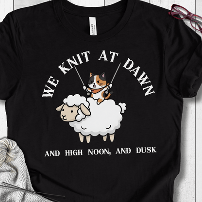 Funny black t-shirt featuring a cat knitting on a sheep, with the phrase 'We Knit at Dawn'.