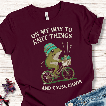 Funny burgundy t-shirt featuring a frog on a bike with knitting supplies, perfect for knitters.