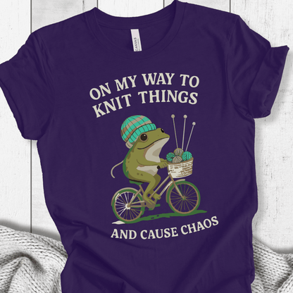 Purple cotton t-shirt featuring a frog on a bike with knitting supplies and humorous text.