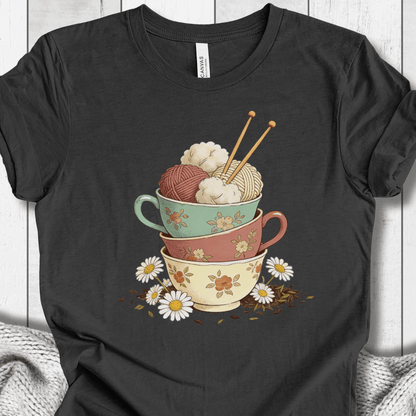 Graphic tee featuring stacked colorful bowls with yarn and knitting needles, on a charcoal background.