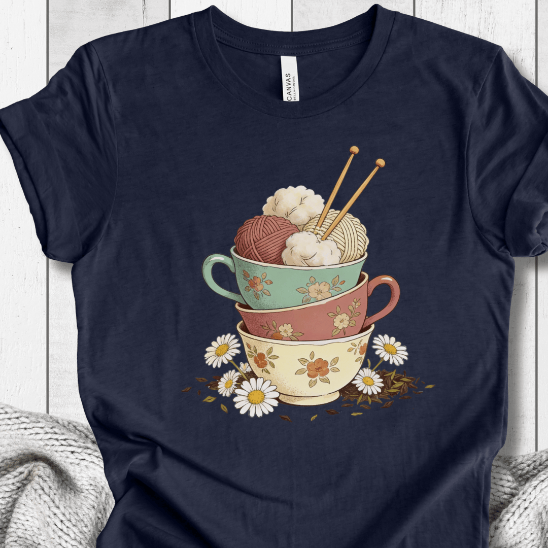 Navy blue t-shirt featuring colorful decorative cups stacked with yarn balls and knitting needles.
