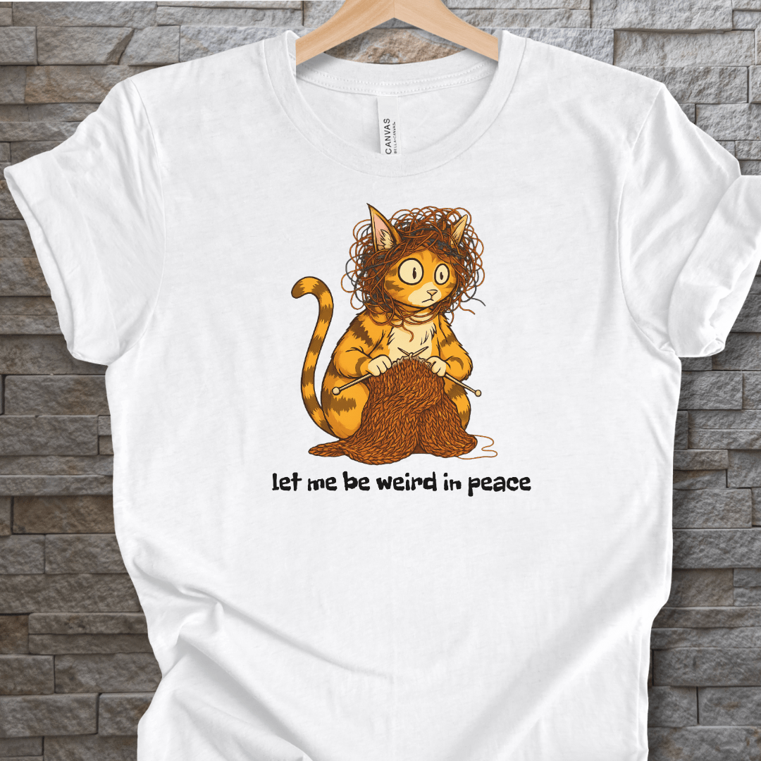 Funny white t-shirt featuring a quirky orange cat with yarn and the text 'let me be weird in peace'