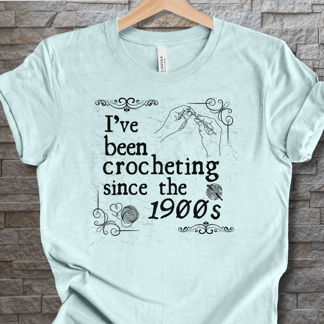 Light blue t-shirt featuring a crochet design with text 'I've been crocheting since the 1900s'.