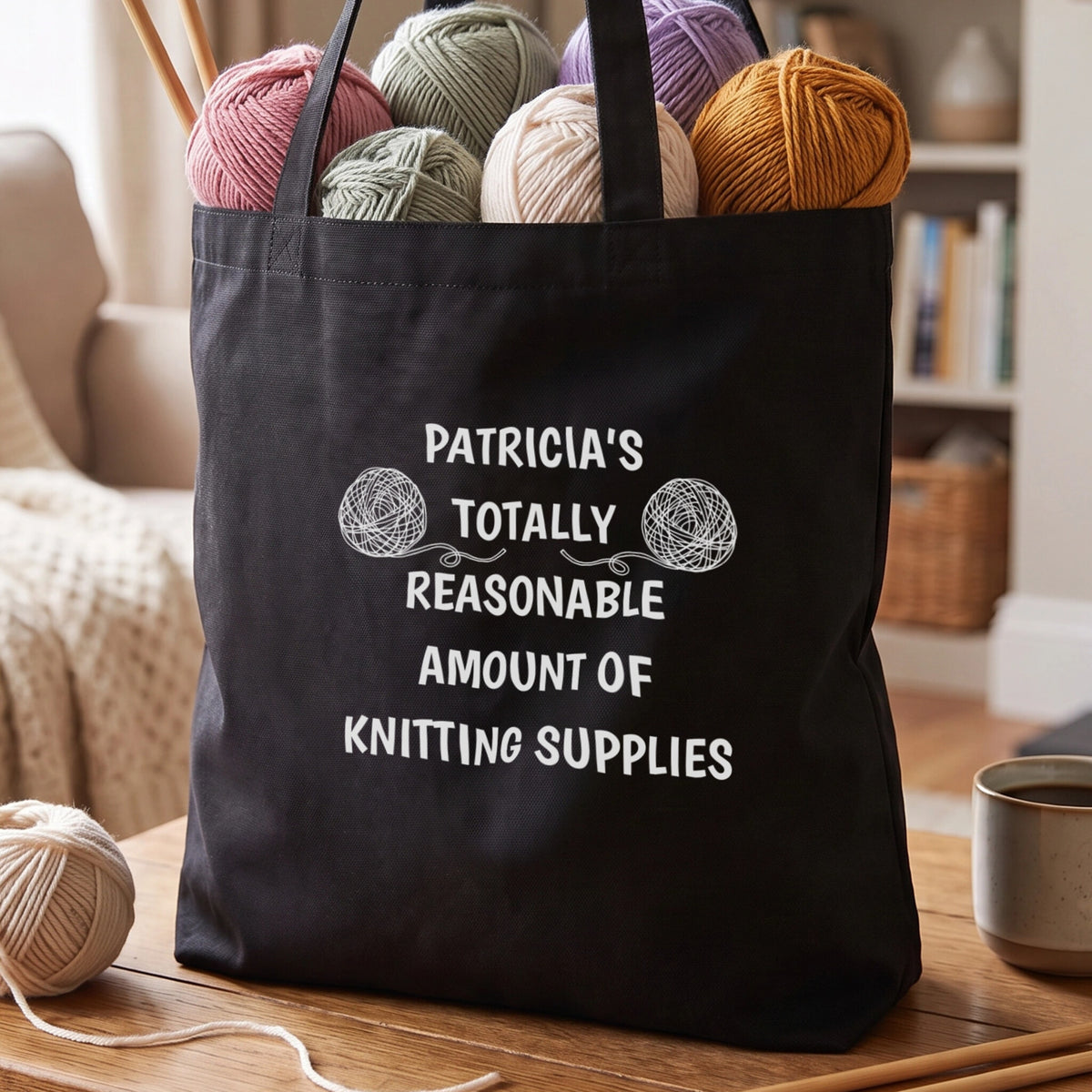 Black tote bag reading Patricia's Totally Reasonable Amount of Knitting Supplies, with two hand-drawn yarn balls